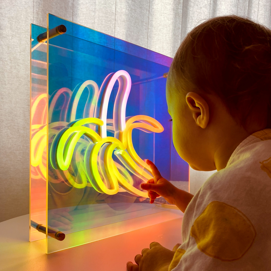 A child interacting with a self-standing infinity mirror box that displays a colorful banana design when illuminated.